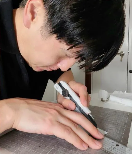 A person leaning over a ruler and cutting mat with a handheld tool